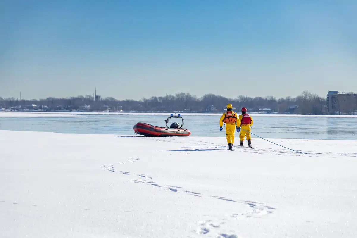 De la glace couverte de neige sur le bord d'un plan d'eau et deux intervenants qui se dirige vers un bateau