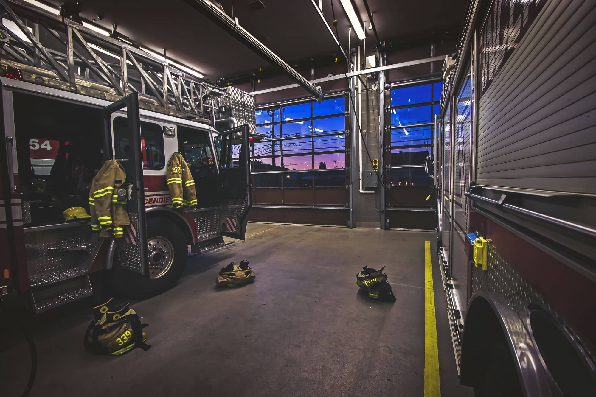Le garage d&#039;une caserne de pompiers avec deux camions de pompier et des uniformes jaunes.
